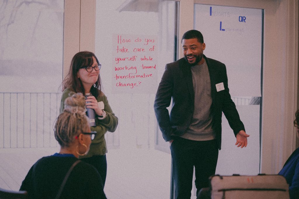 A man and woman present to a group together, as the woman smiles sincerely